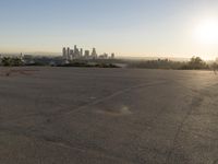 the person riding his bike through the parking lot near a city skyline as he goes off into the distance