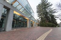 a brick paved sidewalk with large windows and trees in the background on a cloudy day