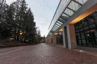 a brick paved sidewalk with large windows and trees in the background on a cloudy day