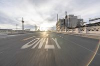 the sun is setting on the road in the city with buildings and street signs in the foreground