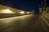 an empty highway next to buildings at night with traffic lights on it and no vehicles in the way