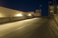an empty highway next to buildings at night with traffic lights on it and no vehicles in the way