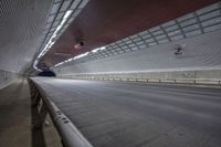 a highway near an elevated rail tunnel, with lights shining brightly over the walkway to the right