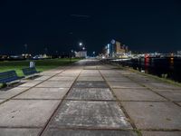 the bench is on a city sidewalk by the water in the night time, the view is incredible