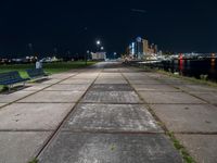 the bench is on a city sidewalk by the water in the night time, the view is incredible