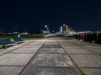 the bench is on a city sidewalk by the water in the night time, the view is incredible