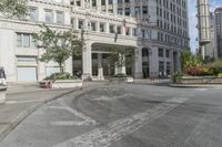 a city intersection with many tall buildings and cars in front of it and people riding around