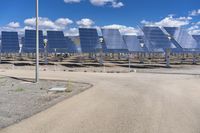 a solar park with rows of shiny blue panels on it's side and the sky behind them