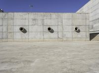 the side of an empty concrete structure with four cement round holes on each side of it