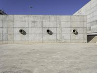 the side of an empty concrete structure with four cement round holes on each side of it