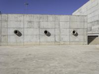 the side of an empty concrete structure with four cement round holes on each side of it