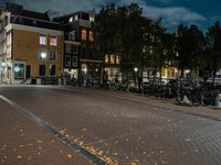 bicycles and lights illuminate the walkway in an otherwise empty city block near many parked buildings