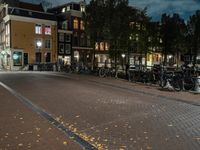 bicycles and lights illuminate the walkway in an otherwise empty city block near many parked buildings