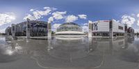 a fisheye view of a square and shopping mall, with clouds in the sky