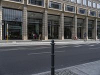 a black pole sitting on the street near a building with many windows and people walking