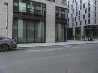 a man riding a motorcycle down a road past tall buildings and cars parked near by