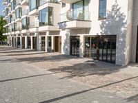 a brick sidewalk outside of a building with glass windows on either side and the street in front of it