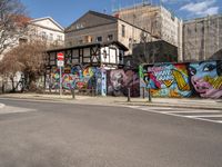 a wall with different colorful artwork on it in a city with buildings around and the street has a bike path going under it