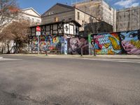 a wall with different colorful artwork on it in a city with buildings around and the street has a bike path going under it