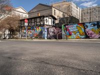 a wall with different colorful artwork on it in a city with buildings around and the street has a bike path going under it