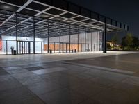 an empty plaza at night lit by low lights and an open walkway with a large window