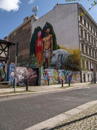 a wall with different colorful artwork on it in a city with buildings around and the street has a bike path going under it