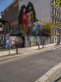 a wall with different colorful artwork on it in a city with buildings around and the street has a bike path going under it
