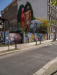 a wall with different colorful artwork on it in a city with buildings around and the street has a bike path going under it