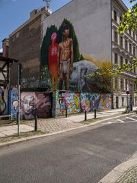 a wall with different colorful artwork on it in a city with buildings around and the street has a bike path going under it