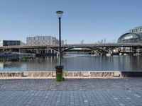 the walkway on the banks of the river, and the city in the background is very tall, with a bridge