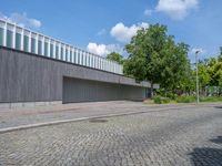 a concrete and brick paved street near a gray building and green trees on either side