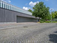 a concrete and brick paved street near a gray building and green trees on either side