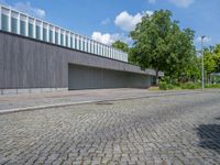 a concrete and brick paved street near a gray building and green trees on either side