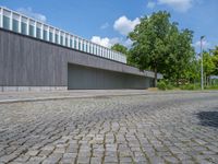 a concrete and brick paved street near a gray building and green trees on either side