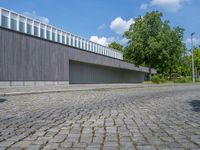 a concrete and brick paved street near a gray building and green trees on either side