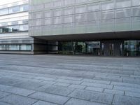 empty plaza with grey stone pavers in front of glass covered building's entrance