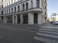 this is a city street corner with cars passing by it and several people on the sidewalk waiting to cross at an intersection