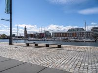 a stone pavement that is near a waterway in a city area with boats docked and buildings in the distance