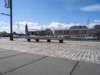 a stone pavement that is near a waterway in a city area with boats docked and buildings in the distance