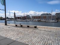 a stone pavement that is near a waterway in a city area with boats docked and buildings in the distance