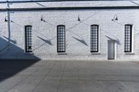 four large windows sit next to each other by the sidewalk of a building, and on which a door opens to allow some light