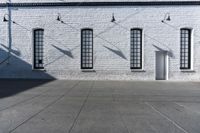 four large windows sit next to each other by the sidewalk of a building, and on which a door opens to allow some light