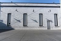 four large windows sit next to each other by the sidewalk of a building, and on which a door opens to allow some light