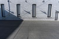 four large windows sit next to each other by the sidewalk of a building, and on which a door opens to allow some light