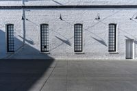 four large windows sit next to each other by the sidewalk of a building, and on which a door opens to allow some light