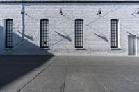 four large windows sit next to each other by the sidewalk of a building, and on which a door opens to allow some light