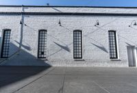 four large windows sit next to each other by the sidewalk of a building, and on which a door opens to allow some light