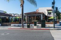 an intersection of town with palm trees in front of a restaurant with umbrellas on the side