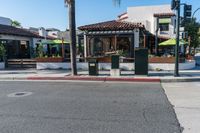 an intersection of town with palm trees in front of a restaurant with umbrellas on the side