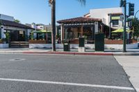 an intersection of town with palm trees in front of a restaurant with umbrellas on the side